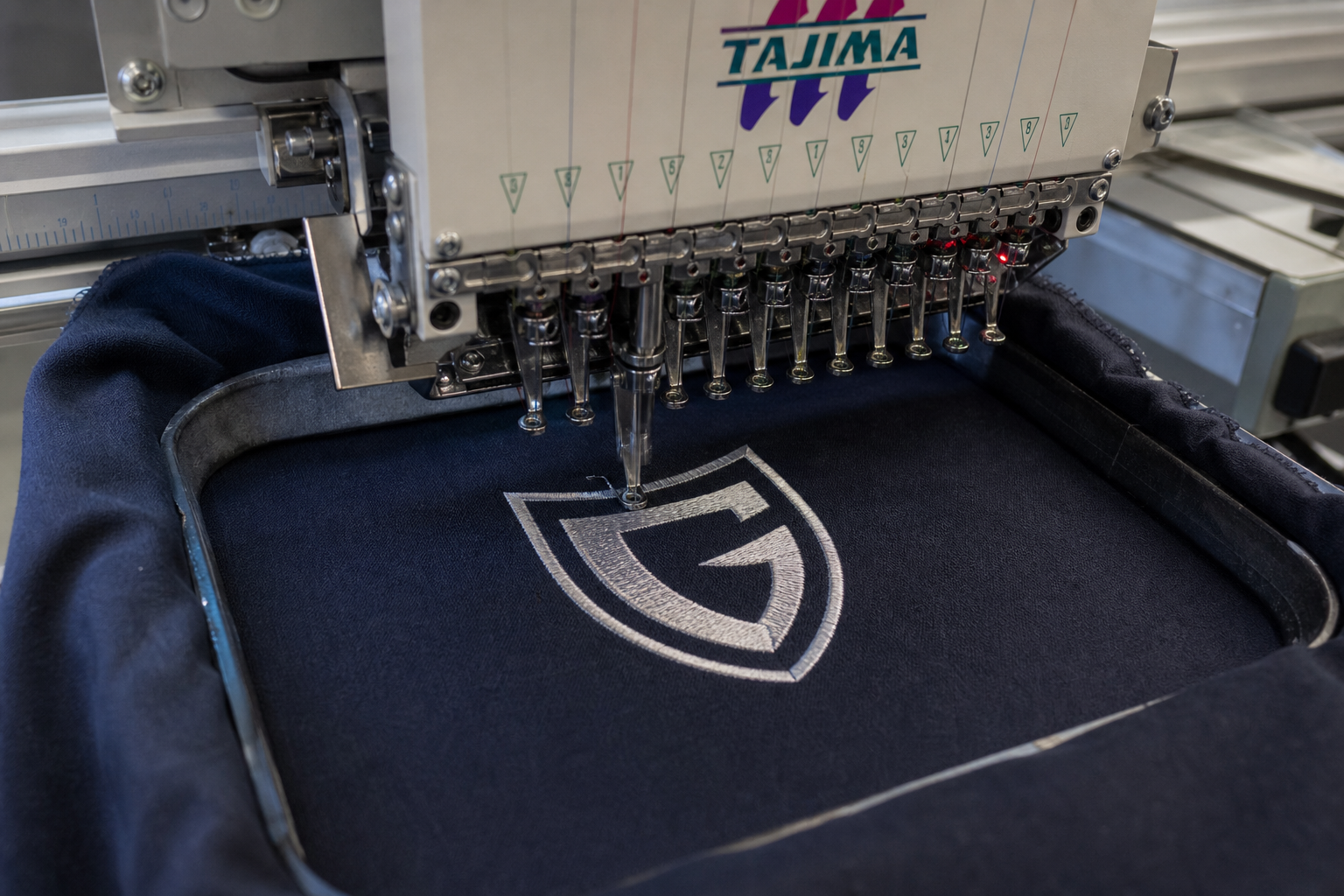 Commercial embroidery machine sewing a logo onto navy fabric