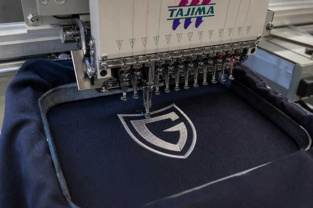Commercial embroidery machine sewing a logo onto navy fabric